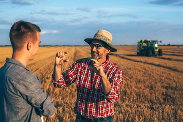 two ranchers talking on field. agricultural machine working in blurred background