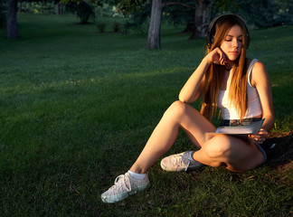 Beautiful blonde girl studying and listening to music in the park. student concept.