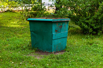 Old rusty metal green garbage container full with waste standing in city park or forest. Environmental pollution