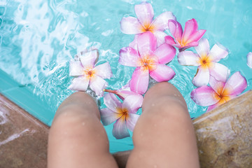 Baby feet in a swimming pool. Tropical flowers Frangipani Plumeria, Leelawadee floating in the water. Spa pool. Peace and tranquility. Spa concept.