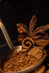Stick of cinnamon and oriental spices, aniseed cocoa, with a vintage spoon of ground coffee and unroasted grains on a dark background. free space for your text. Close-up macro image.