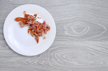 Beer snack on a white plate on a background of gray, wooden table. Smoked pork ears close-up.