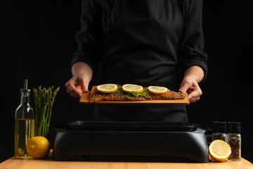 Cooking by a chef seafood, grilling red fish, salmon or trout on a black background. Movement, restaurant menu, recipe book, Asian cuisine, homemade recipe. Horizontal photo