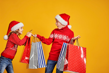 Cute little girl in Santa hat hanging shopping bag with Christmas gifts on hand of astonished boy...