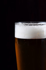 Beer with foam in a tall glass against black background