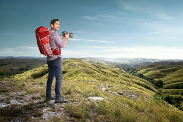 Asian man with a backpack holding a camera to take pictures