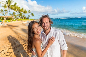 Happy couple on romantic sunset beach stroll walking on honeymoon Hawaii winter escape holiday. Smiilng Asian woman and Caucasian man, biracial couple.