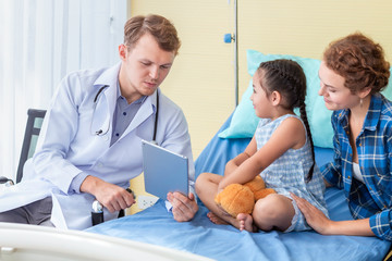 Pediatrician (doctor) man recording and taking information to tablet with little girl patient and mother in hospital.