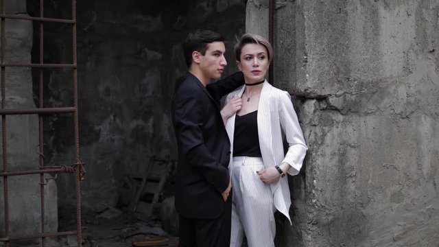 beautiful model with short fair hair fixes jacket and poses with handsome partner at concrete wall slow motion