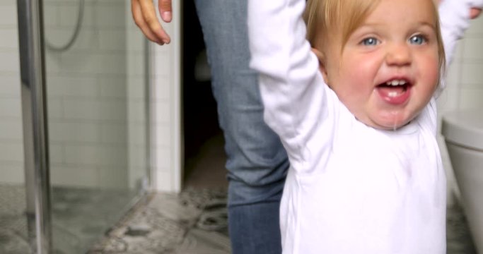 Cute happy little toddler learning walking with help of grown up in bathroom