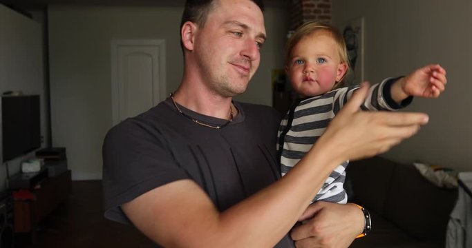 Irritated toddler with eyebrows frowned lips pursed in fathers hands looking at camera