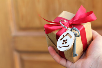 hand with a gift decorated with a small house and a key on the background of the door. real estate offer