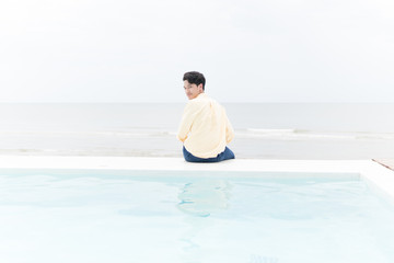 Fototapeta na wymiar A young man sitting quietly at the pools edge overlooking the ocean