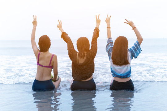 Group of three happy people sits on background of empty sunset beach. Travel or sea vacations concept - Powered by Adobe