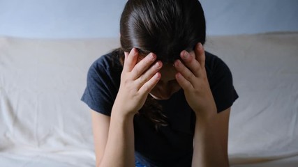 Depressed anxious worried young woman sitting on the sofa crying at home. Depressed frustrated female having emotional problems, fears, worried and hopeless. Psychological therapy, no energy