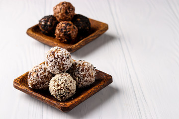Healthy energy balls of nuts, oatmeals and dried fruit with coconut, flax and sesame seeds on wooden coconut plates on a white background, horizontal orientation