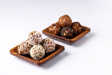Healthy energy balls of nuts, oatmeals and dried fruit with coconut, flax and sesame seeds on wooden coconut plates on a white background, horizontal orientation