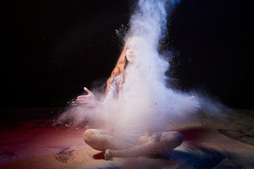 Fototapeta premium Beautiful teen girl with long blonde curly hair in a dark room with colored lights and clouds of flour