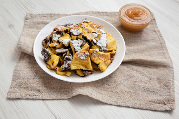 Homemade german Kaiserschmarrn pancake with apple sauce on a white wooden surface, side view. Close-up.