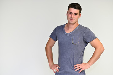 Obraz premium Portrait of a handsome young man with black hair in a blue and gray t-shirt on a white background. Shows emotions in various poses, talking.