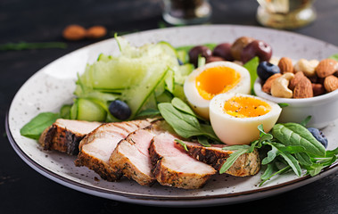 Ketogenic diet. Keto brunch. Boiled egg, pork steak and olives, cucumber, spinach, brie cheese,...
