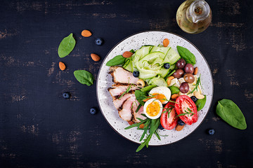 Ketogenic diet. Keto brunch. Boiled egg, pork steak and olives, cucumber, spinach, brie cheese, nuts and tomato. Top view