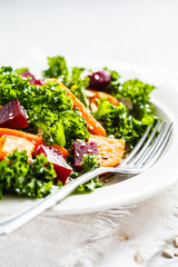 Kale salad with baked vegetables in white plate.
