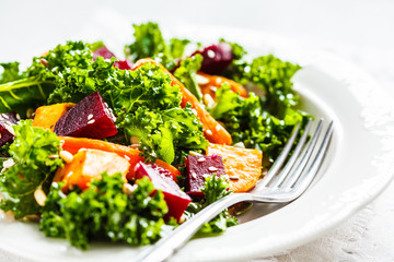 Kale salad with baked vegetables in white plate.