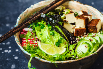 Poke bowl with avocado, black rice, smoked tofu, vegetables, sprouts, dark background.