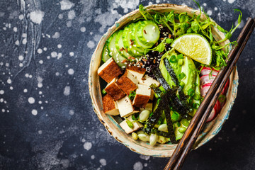 Poke bowl with avocado, black rice, smoked tofu, vegetables, sprouts, dark background.