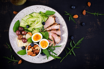 Fototapeta na wymiar Ketogenic diet. Keto brunch. Boiled egg, pork steak and olives, cucumber, spinach, brie cheese, nuts and blueberry. Top view