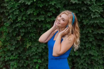 Beautiful young blonde girl in a dress listening to music in blue headphones. Real life, enjoy the moments. Copy space.