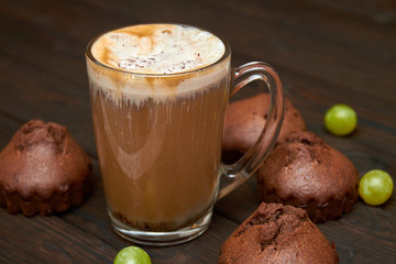 A cup of iced coffee with homemade chocolate muffins and grapes on dark wooden background. Closeup, selective focus