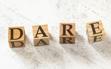 Four wooden cubes with letters DARE (stands for decision-making model -Define, Assess, Respond, Evaluate) on white working board.