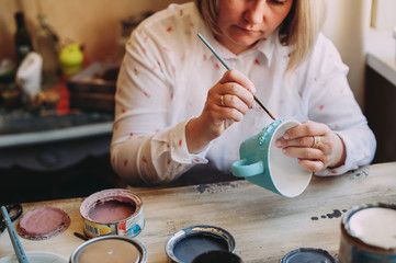 Fototapeta na wymiar Woman working In her pottery studio. Ceramic workshop. Paint on clay mug in the pottery.