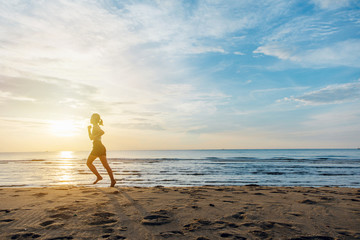 Silhouette of an athletic woman running on the beach during sunset time