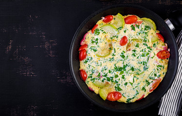Omelette with tomatoes, zucchini and red onion on dark table.  Frittata - italian omelet. Top view