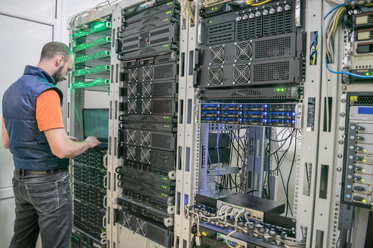 Young man diagnoses problems in the work of the information center. System administrator uses a laptop to check the server hardware. A software engineer is working in a modern data center.