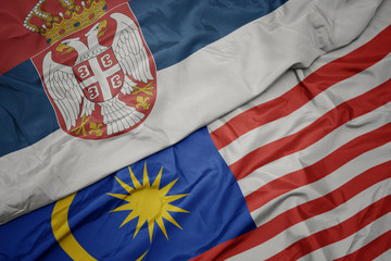 waving colorful flag of malaysia and national flag of serbia.