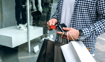 Young man with shopping bags taking out credit card from wallet