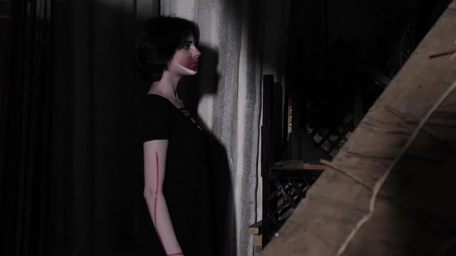 attractive sad woman with artistic makeup in black dress comes to light wall from darkness among decorations slow motion