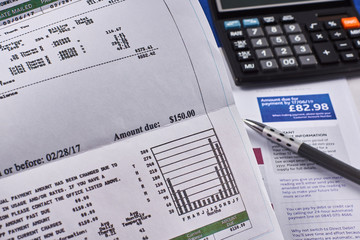 Comparison of utility bills in dollars and pounds. Utility bill sheets, calculator and pen. Close-up