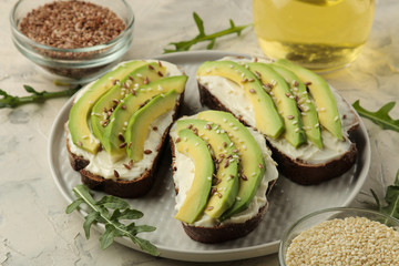 A sandwich of cream cheese bread, and slices of avocado on a plate on a light concrete background. making sandwiches.