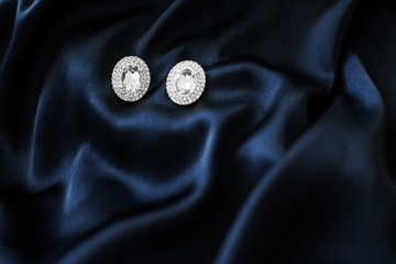 Luxury diamond earrings on dark blue silk background, holiday glamour jewelery present