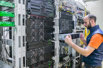 A man works in a server room. System administrator installs a new server in a modern data center.  The engineer replaces the computer equipment in the cabinet. A technician repairs the central router.