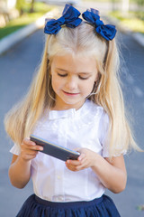 Beautiful elegant cheerful girl goes to elementary school with an apple, a book and a phone