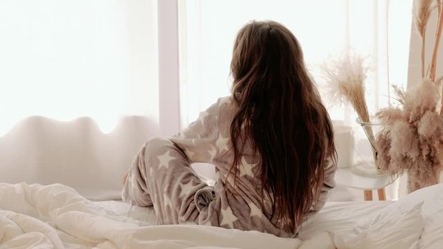 Cozy morning. Healthy comfortable rest. Teenage girl in pajamas waking up leaving bed.