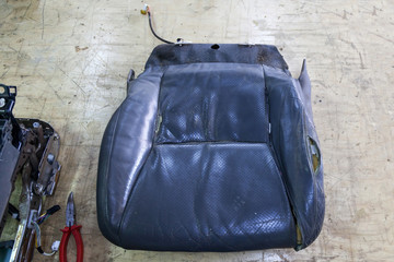 An old car seat made from tattered and torn leather upholstery on a workbench in a workshop for the...