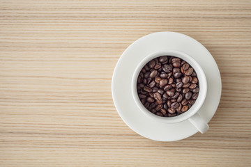 fresh roasted coffee beans in white cup on wood table, top view