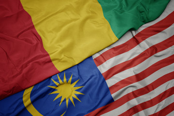 waving colorful flag of malaysia and national flag of guinea.